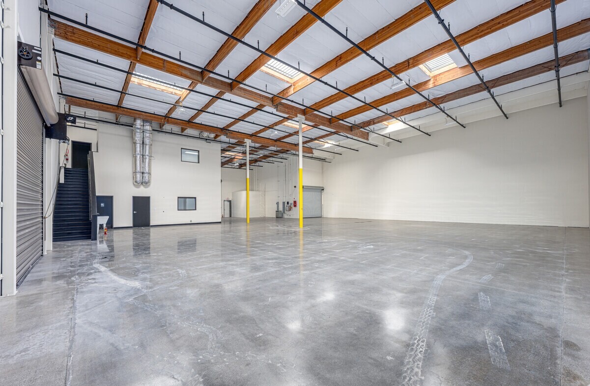 Open warehouse with exposed wood trusses, skylights, mezzanine stair and polished concrete slab